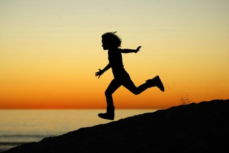 A boy runs down a sand dune