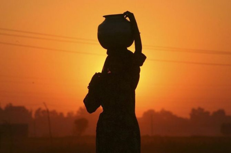 A Gujjar or nomad woman carrying a pitcher filled with drinking water is silhouetted against the setting sun on the outskirts of Jammu December 3, 2011.