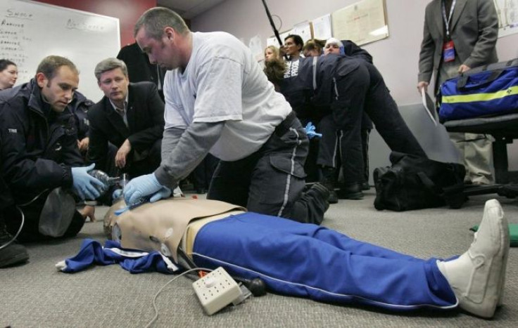 Conservative Party of Canada leader Stephen Harper (2nd L) watches as paramedic students Tris Windfield (L) and Judd Stevenson (R) practise resuscitation using a training dummy, while promoting his education and training for young Canadians, in North Bay