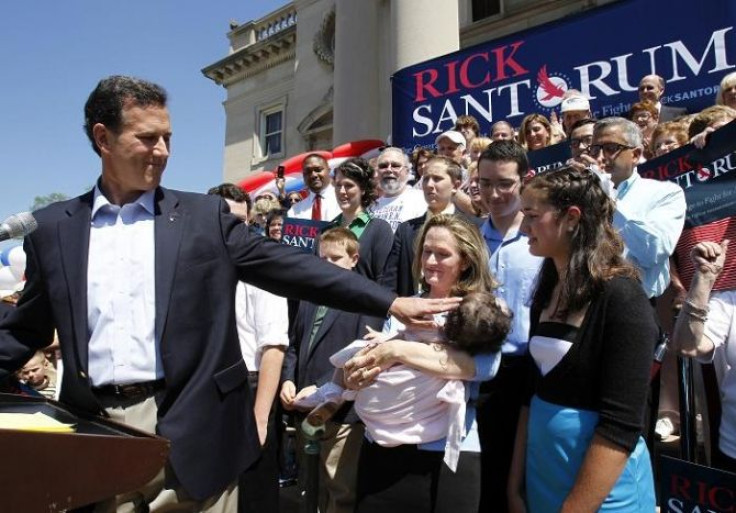 Former U.S. Senator Rick Santorum (C) hands his daughter Isabella Maria (bottom) off to a family friend after she threw up on him as his wife Karen (L) was introducing him during a rally to officially announce his candidacy for President of the United Sta