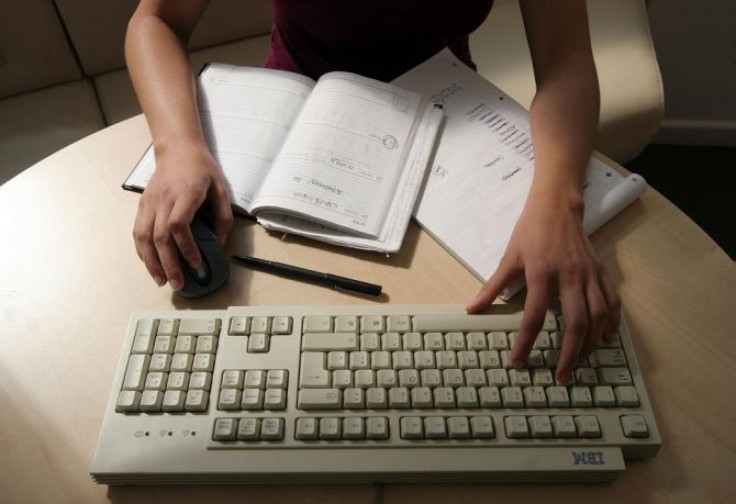 A generic picture of a woman sitting at her desk typing on a computer.