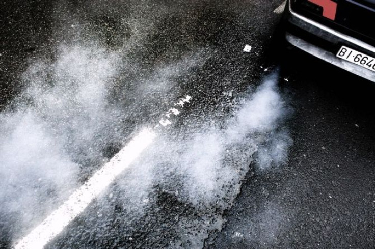 A car produces smoke from its exhaust as it pulls away.