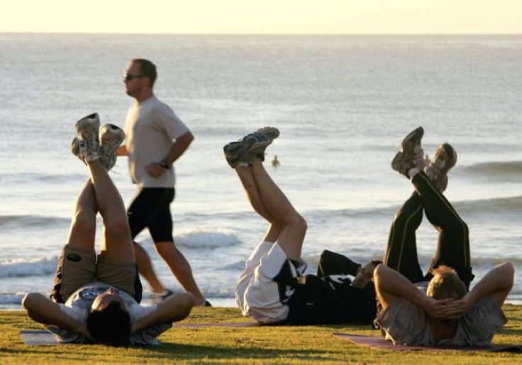 Jogger passes fitness enthusiasts performing stretching exercises after sunrise at Queenscliff Beach in Sydney