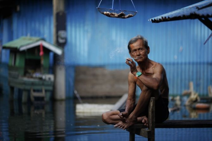 An elderly man smokes a cigarette outside his flooded home in a slum just outside Bangkok