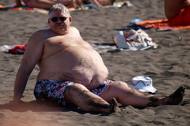 Obese man sits at the beach