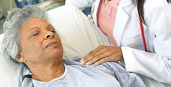 A woman in bed being aided by physician