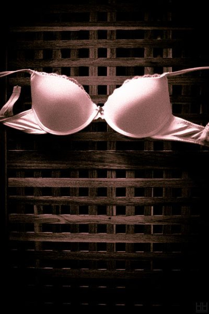 Pink bra hanging on wooden structure.