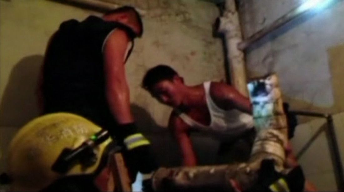Firefighter handing sewage pipe to his colleague.