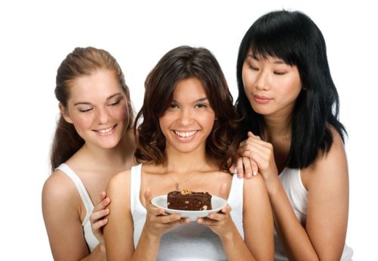 Woman holding a piece of cake with friends looking over her shoulder