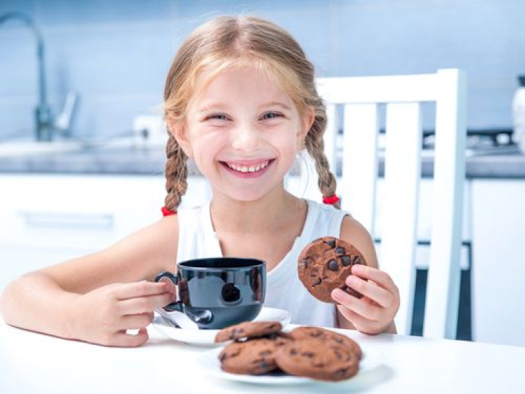 Little girl eating cookies and having tea in kitchen