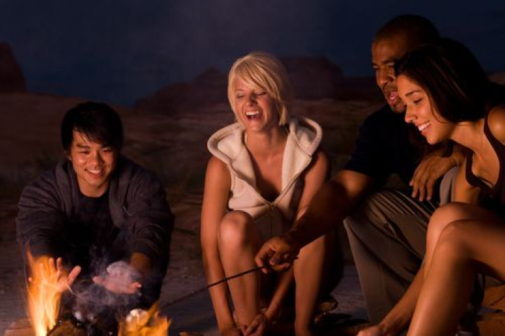 People sitting around a campfire at night roasting marshmallows