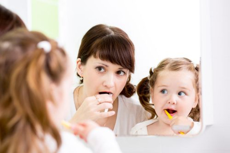 Mother teaching daughter how to brush teeth in front of mirror