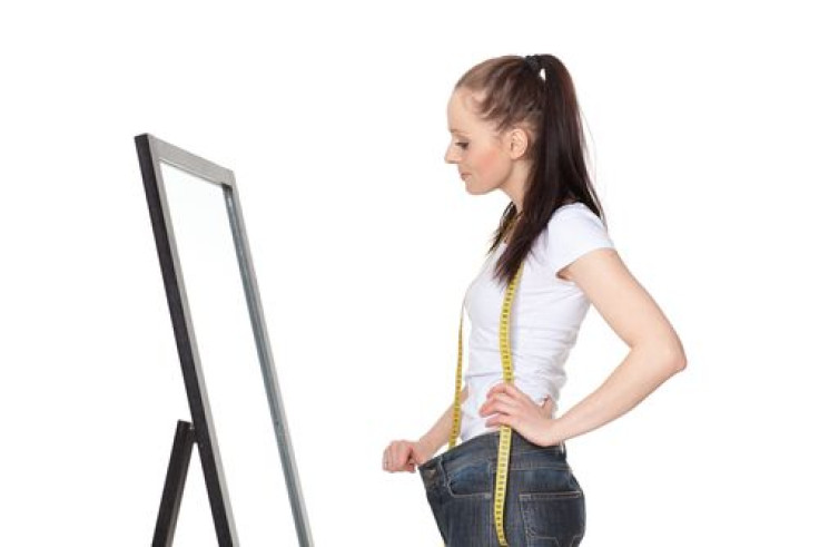 Woman looking in mirror wearing old jeans after losing weight