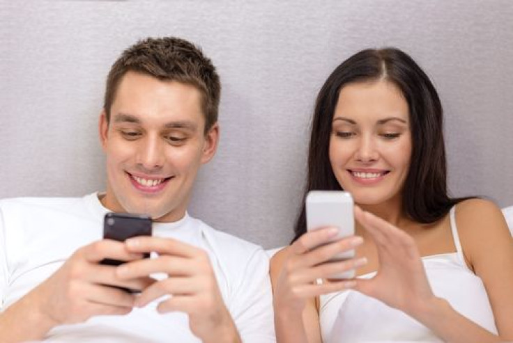 Happy couple in bed using smartphones