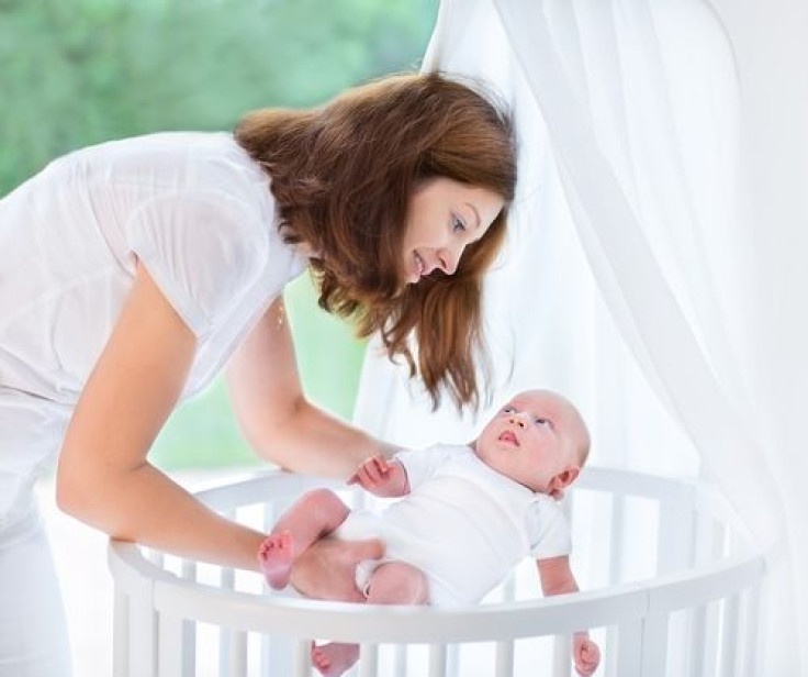 Mother putting newborn baby into white crib