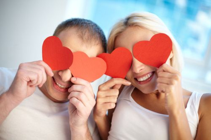 Happy couple holding paper hearts by their eyes