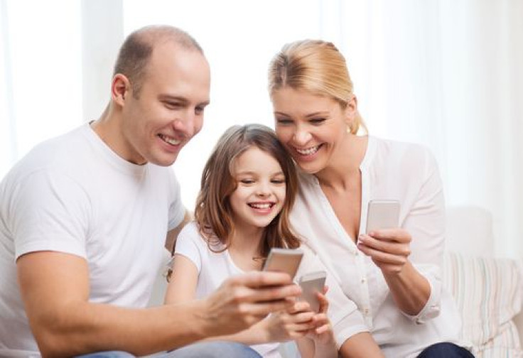 Smiling parents and child holding electronic devices in their hands