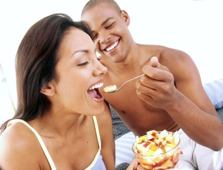 Young couple enjoying and eating fruit salad on bed