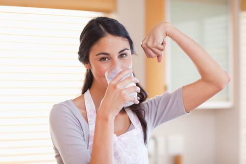 Woman drinking milk and flexing arm muscle 