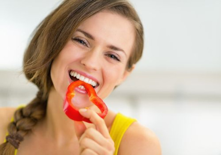 Happy woman eating bell pepper in kitchen