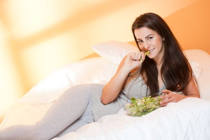 Woman eating bowl of salad in bed