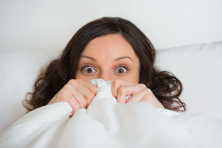 Woman  hides her face in bed and looking at camera with wide eyes