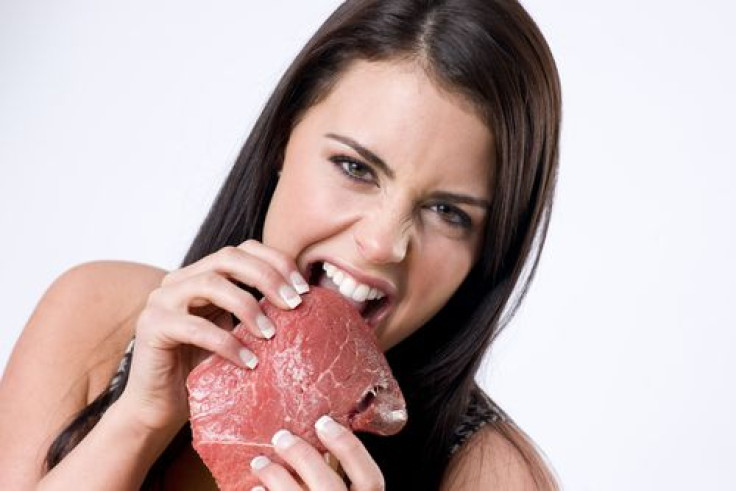 Woman ripping raw red sirloin steak with teeth