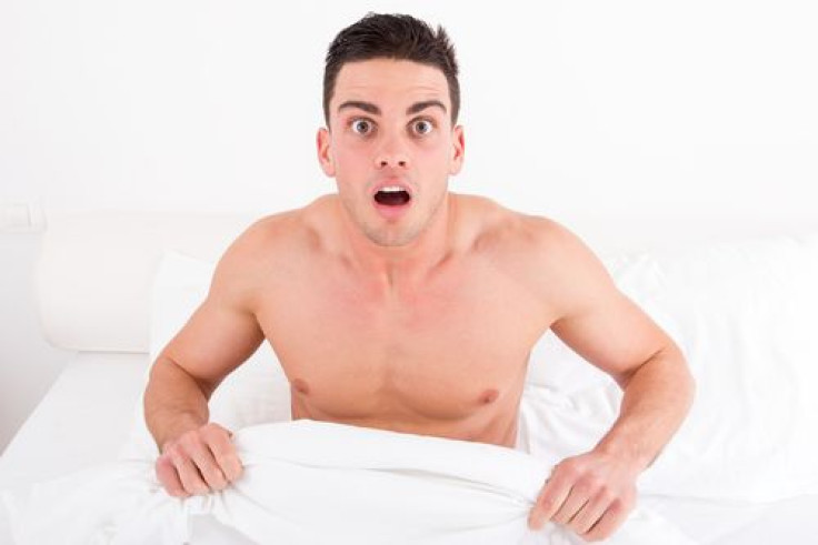 Surprised and shocked half naked young man in bed looking down at his penis 