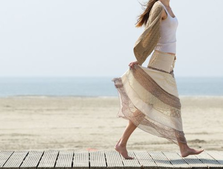 Woman walks barefoot on beach with dress