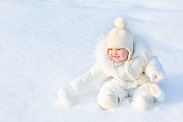 Baby girl sitting in white snow wearing a warm jacket and knitted hat