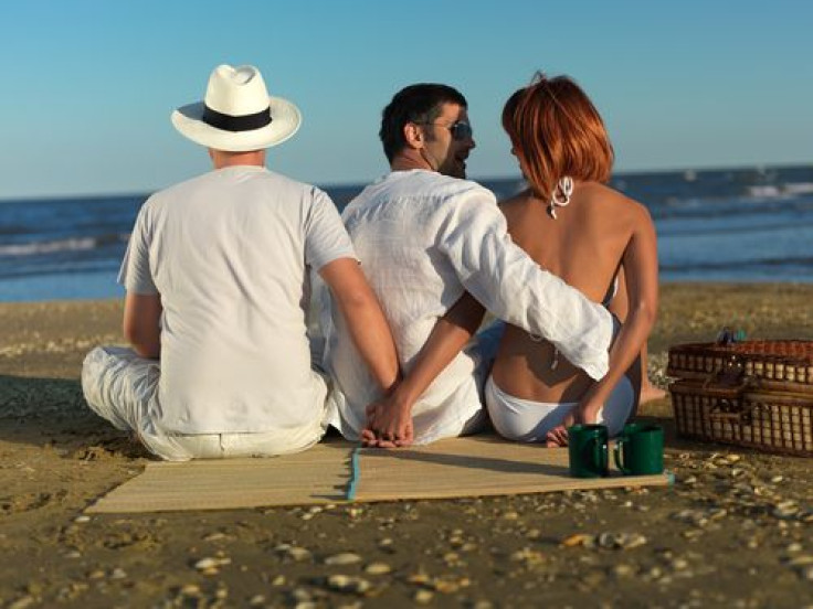 Woman talking with the boyfriend, while holding hands with another man, at a picnic by the sea shore