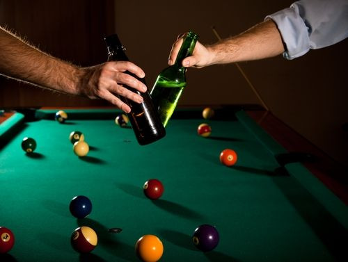 Men clinking beer over pool table