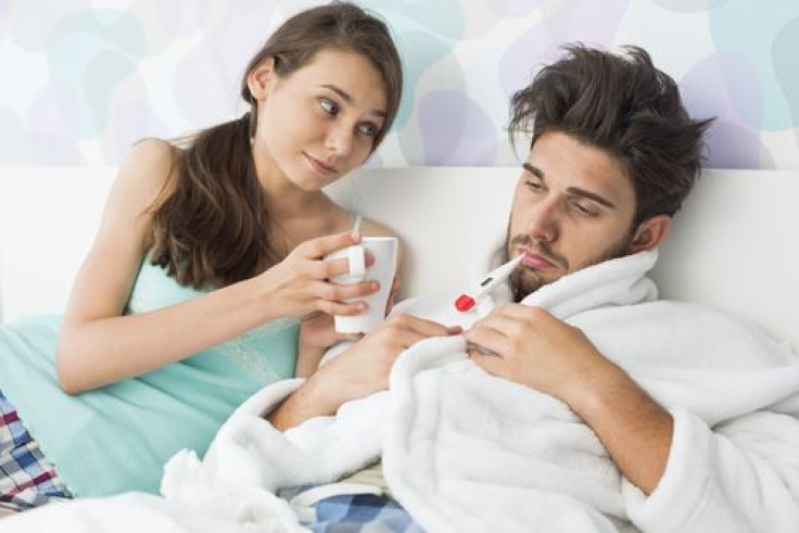 Woman giving coffee mug to man with thermometer in mouth