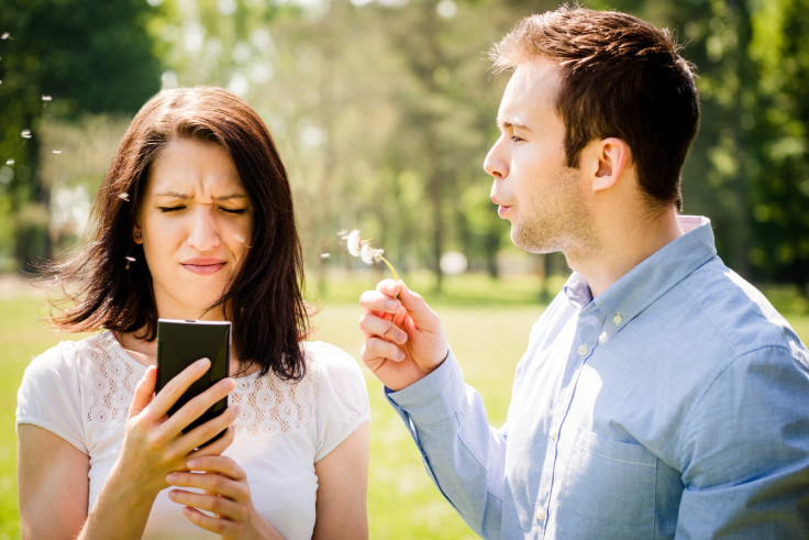 Young man blowing dandelion to face of angry woman holding mobile phone