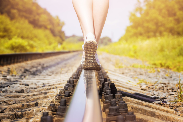 Woman in sneakers on the rail of the railway