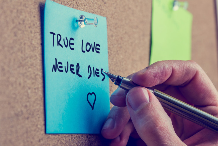 Man writes true love never dies phrase on post it paper on cork bulletin board 