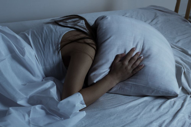 Girl covers head with pillow while laying in bed