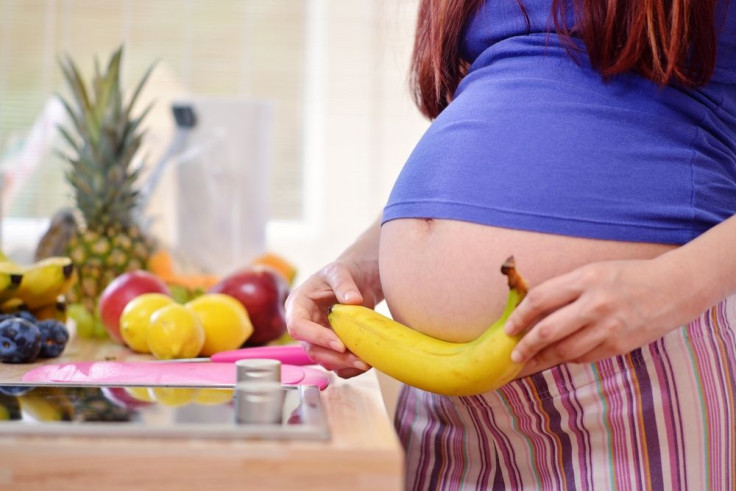 Pregnant woman holding banana in kitchen