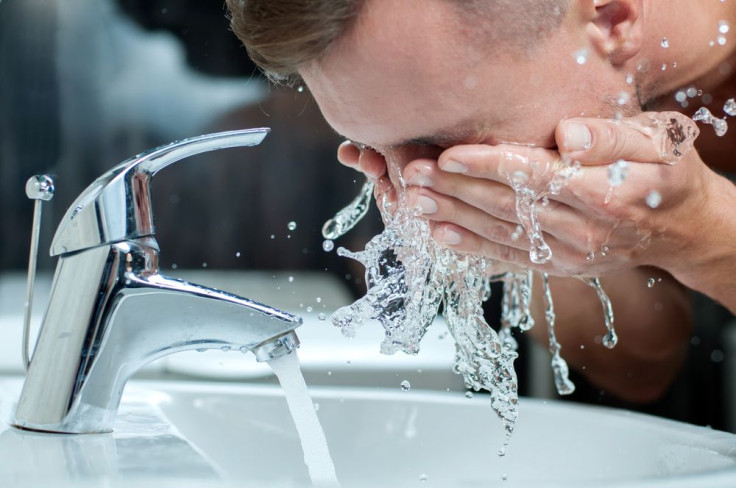 Man washing face over faucet 