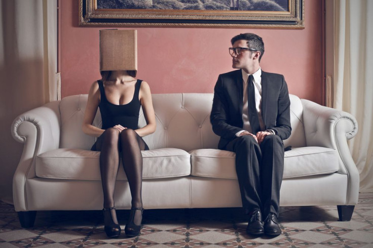 Man looks at woman with box on head sitting on couch