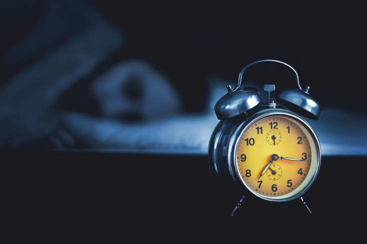 Young man sleeping in the bed with alarm clock on table