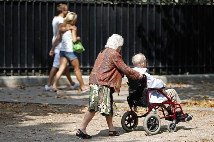 An elderly woman pushes a man in a wheel chair.