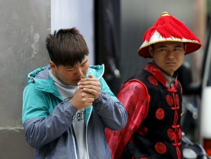 An Asian man lights a cigarette as his friend watches. 