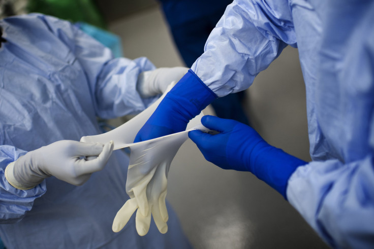 A nurse helps a doctor put on a pair of gloves. 