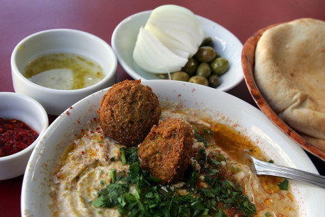 A bowl of hummus is served with olive oil, falafel balls and sprinkled with chopped parsley alongside fresh-baked pita bread, olives, a fresh onion, red chili paste and chili and lemon juice February 21, 2006 in a restaurant in Tel Aviv.