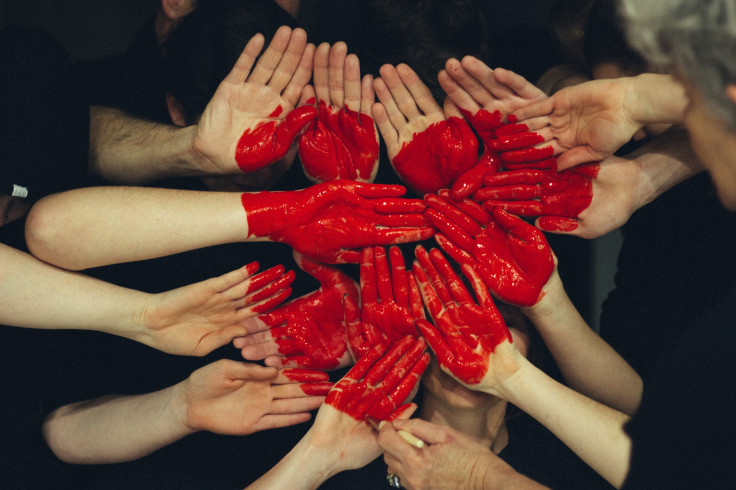 Hands with red paint forming heart