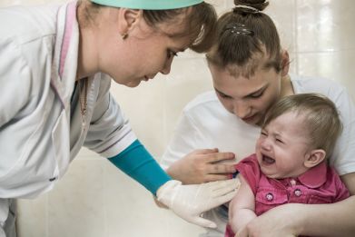 Sonya Yanchuk, age 1, sits in her mother Nadia Yanchuk's lap as nurse Mariana Gonchara (L) administers a measles vaccine shot in health clinic № 10 on May 15, 2019 in Kiev, Ukraine.