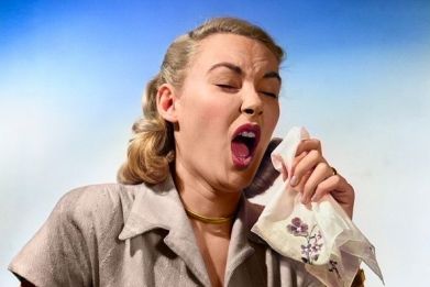 A 1950s woman sneezing and coughing into handkerchief.