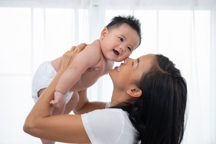 A laughing mother lifting her adorable newborn 